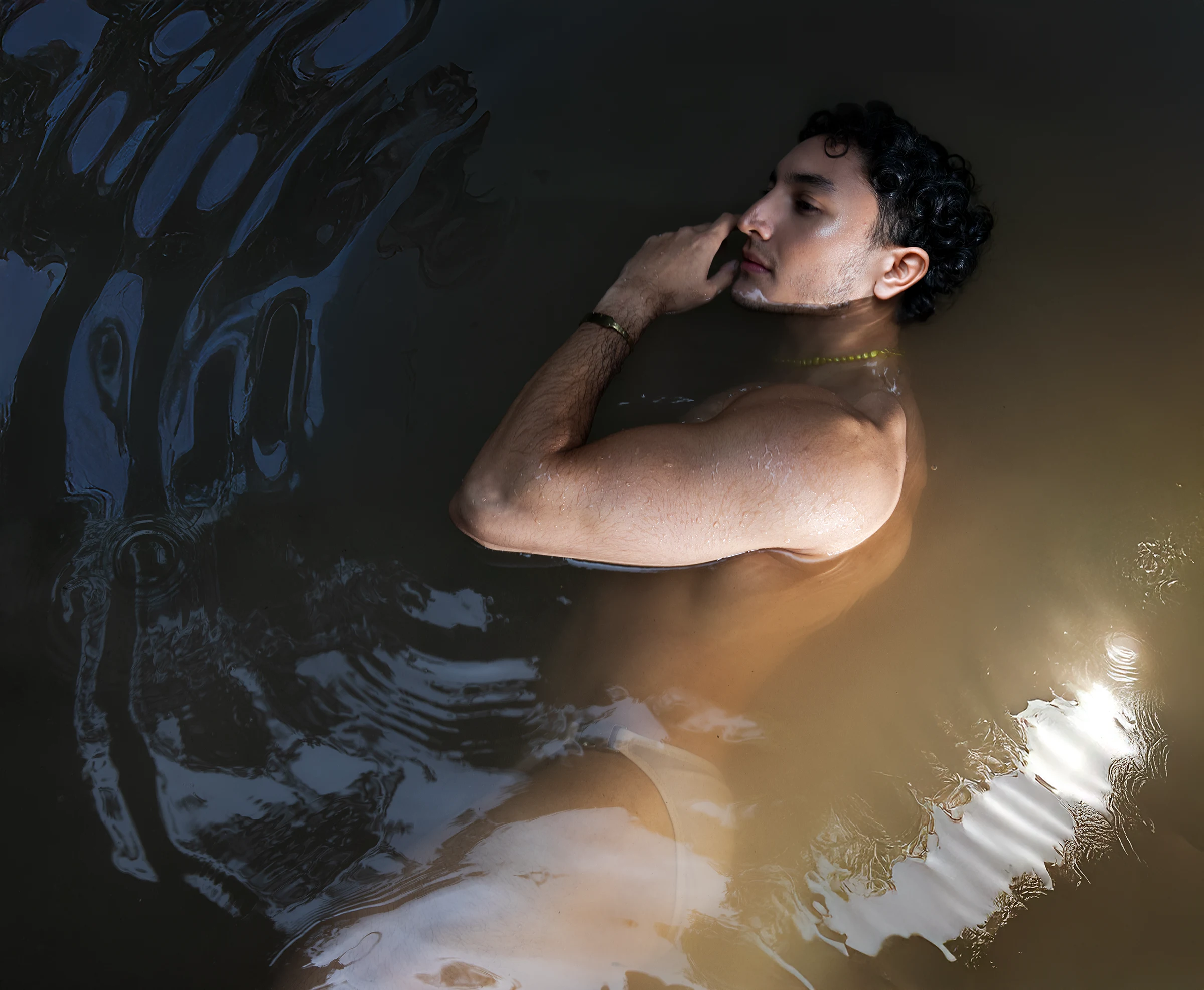 Luian sumergido en agua oscura en Tolantongo usando joyas SERGIO STUDIO.