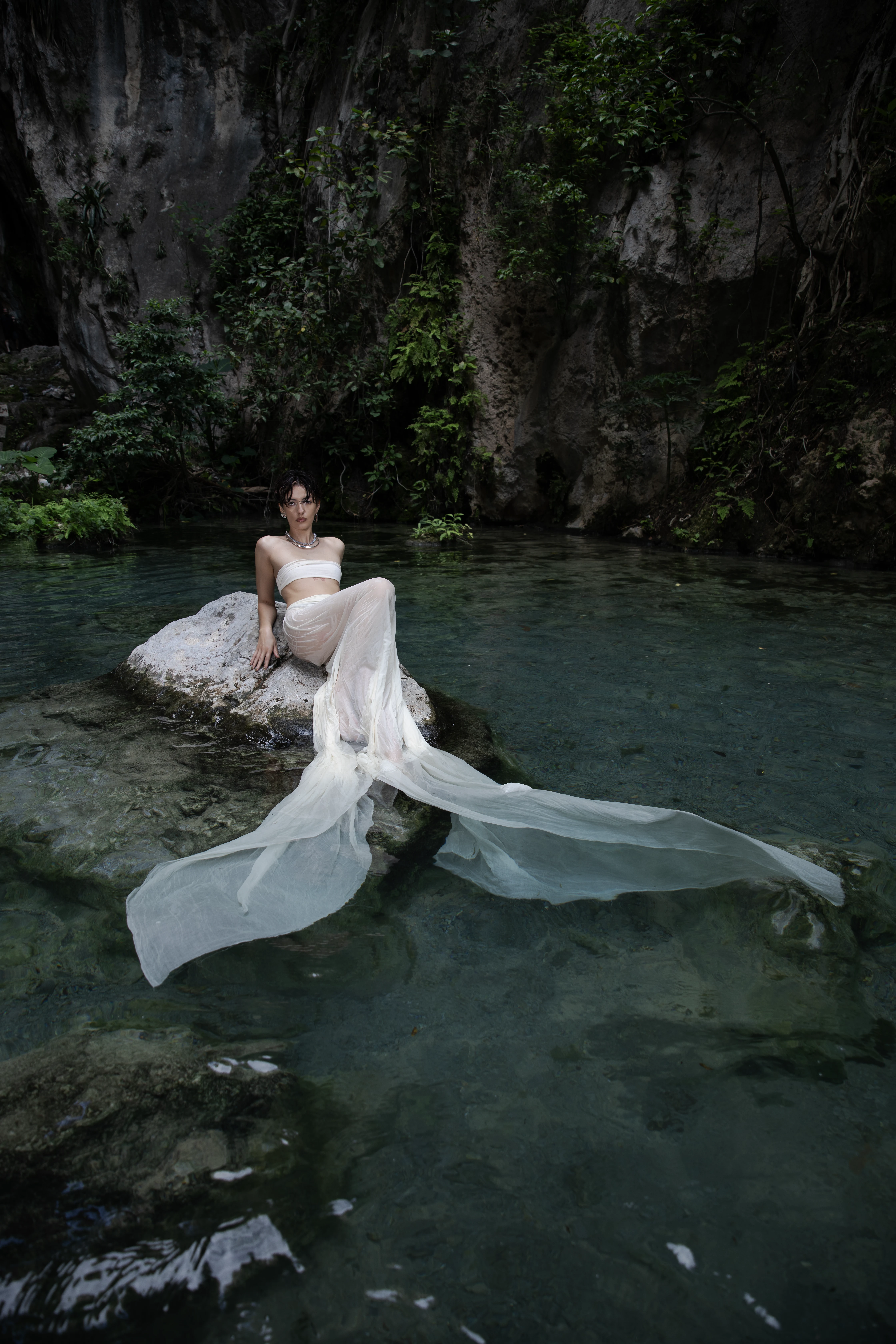 A woman in a white dress seated in the river at Tolantongo.